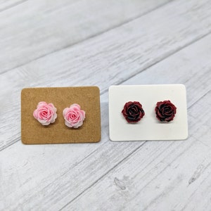 May include: Two pairs of rose-shaped earrings on display cards. One pair is pink and the other is burgundy.