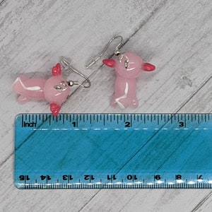 以下が含まれることがあります： ピンクのアホロートルイヤリングのペア。各イヤリングは、赤いエラと白いアクセントが付いた、小さく半透明のピンクのアホロートルが特徴です。イヤリングは、銀色のフィッシュフックのイヤワイヤーから吊り下げられています。イヤリングの長さは約2.5cmです。