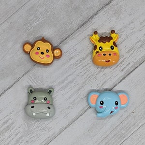 May include: Four colorful animal face figurines. A brown monkey, a yellow giraffe, a gray hippopotamus, and a blue elephant. Each figurine has a smiling face with black eyes and pink cheeks.