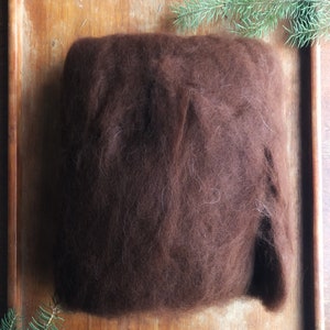 May include: A large amount of brown wool fiber in a wooden tray. The wool is loose and fluffy, and it appears to be ready for spinning or felting.