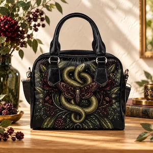 May include: A black handbag featuring a central graphic of a coiled green snake and a moth with a skull pattern on its wings. The design is surrounded by dark foliage, deep red flowers, and berries, with two black handles and gold-tone hardware.