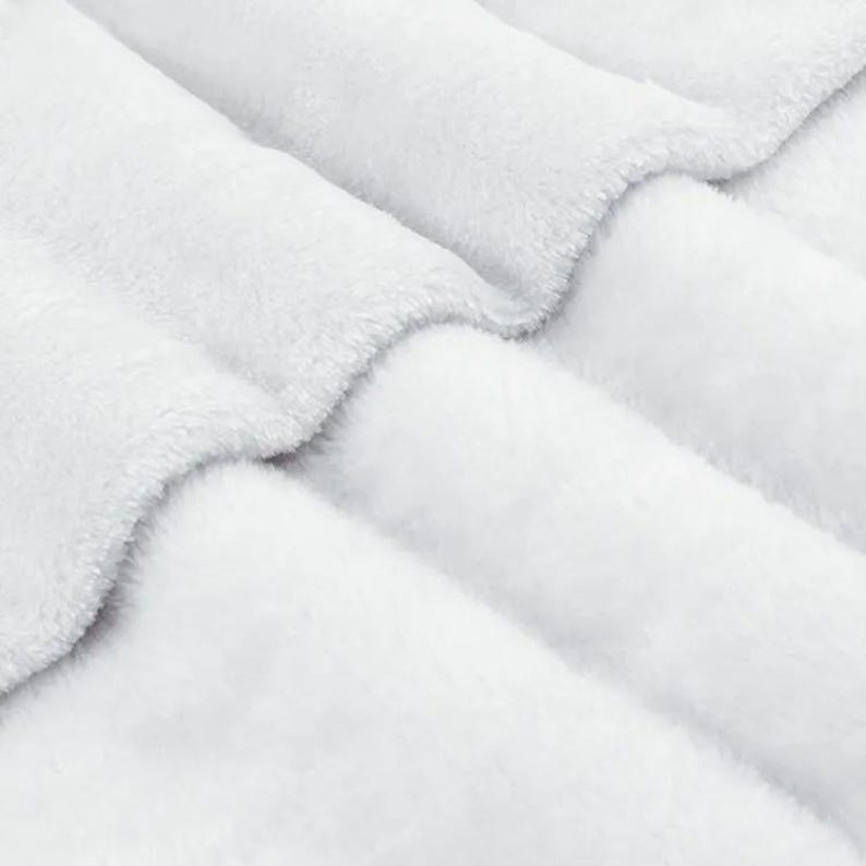 A close-up view of a soft, fluffy white fabric, possibly a blanket or cushion, with a textured and wrinkled appearance.