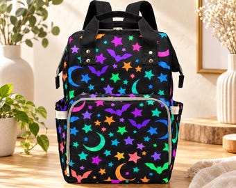 May include: A black backpack featuring a vibrant, repeating pattern of neon-colored bats, crescent moons, and stars in shades of pink, purple, orange, blue, and green. The bag includes a top handle, adjustable shoulder straps, and a front pocket.