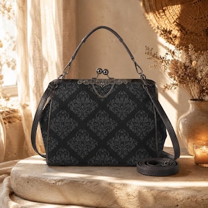 May include: Black handbag with a decorative clasp and a patterned design. The bag has a top handle and a detachable shoulder strap. The bag is sitting on a stone surface.