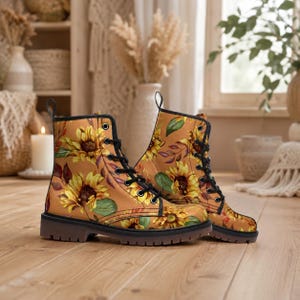 May include: A pair of ankle boots with a sunflower pattern. The boots have a tan background with yellow sunflowers, green leaves, and purple accents. They feature black laces, black eyelets, and a brown sole.