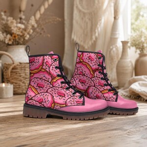 Op de afbeelding: Een paar enkelhoge veterschoenen met een herhalend patroon van roze geglazuurde donuts met kleurrijke hagelslag. De schoenen hebben zwarte veters, zwarte oogjes, een effen roze neus en een dikke, donkerbruine rubberen profielzool.