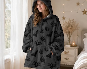 Op de afbeelding: Een donkergrijze oversized hoodie met een vleermuismotief, met een capuchon met kattenoren en een voorzak. De hoodie heeft een halve ritssluiting en is gemaakt van een zacht, pluche materiaal.