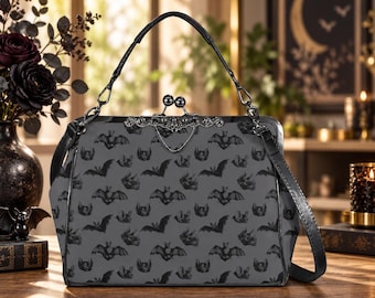 May include: A grey handbag featuring a repeating black bat pattern, a black top handle, and a decorative silver-toned metal kiss-lock clasp. The bag has a structured frame design with black trim and hardware accents.