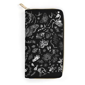 A flat view of the black zippered wallet adorned with white sketches of moths, bones, and hands.