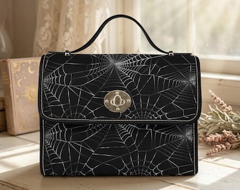 May include: A black handbag featuring a white spiderweb pattern across the entire exterior. The bag has a single top handle, a rectangular flap, and a silver-toned metal twist-lock closure centered on the front. The design includes white stitching.