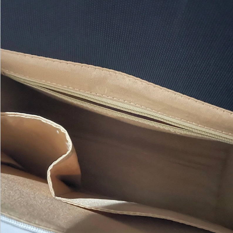 The beige fabric interior of an open bag revealing a zippered pocket and divided slide pockets.