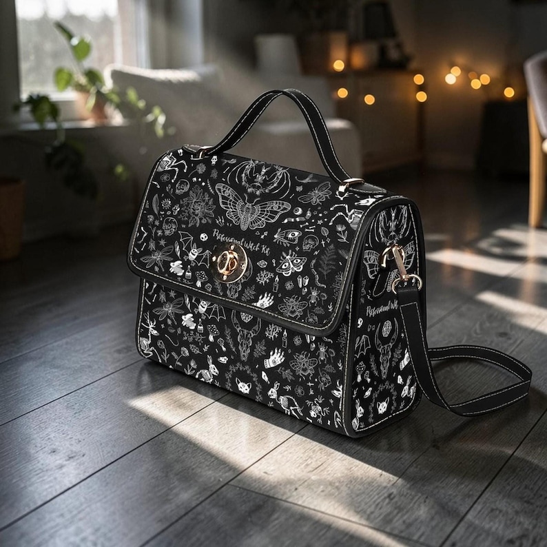 An angled shot of the black handbag showing its carrying strap and side hardware on a wooden floor.