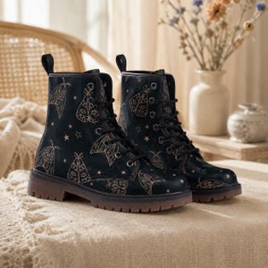 May include: A pair of black lace-up boots featuring a repeating pattern of light-colored moths and small stars. The boots have a rounded toe, a pull tab at the heel, black laces, silver-toned eyelets, and a thick, dark brown lugged rubber sole.