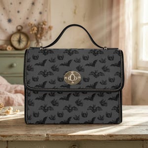 May include: A black handbag featuring a repeating bat pattern. The bag has a black handle and trim, a gold-coloured clasp, and white stitching. The bag is placed on a wooden surface.