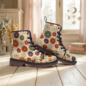 Może przedstawiać: Para beżowych butów bojowych z kolorowym wzorem stokrotek. Buty mają czarne sznurowadła, czarne wykończenie i brązową podeszwę. Kwiatowy wzór zawiera białe, pomarańczowe, fioletowe i niebieskie kwiaty.