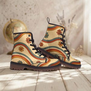 Może przedstawiać: Para beżowych butów bojowych z retro kwiatowym i falistym tęczowym wzorem. Buty mają czarne sznurowadła, czarny kołnierz i brązową podeszwę. Projekt zawiera pomarańczowe, niebieskie i zielone akcenty.