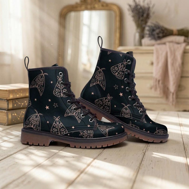 May include: A pair of black lace-up ankle boots featuring a repeating pattern of light-colored moths and small stars. The boots have dark brown soles, metal eyelets, and a pull tab at the back of the collar, constructed with a smooth exterior finish.