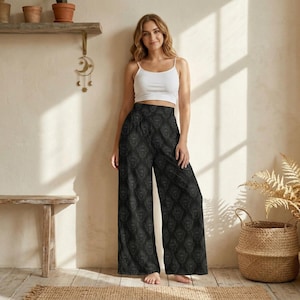 Könnte beinhalten: Ein weißes ärmelloses Tanktop kombiniert mit einer hoch taillierten weiten Hose mit einem dunkelgrauen und schwarzen Damastmuster. Die Hose hat eine lockere Passform und ein durchgehendes, sich wiederholendes ornamentales Design.