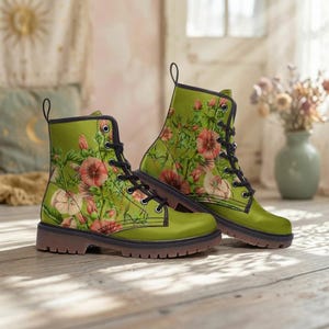 Może przedstawiać: Zielone buty wojskowe z kwiatowym wzorem z różowych i białych kwiatów oraz zielonych liści. Buty mają czarne sznurowadła, czarne wykończenie i brązową podeszwę. Buty są wykonane z gładkiego materiału.