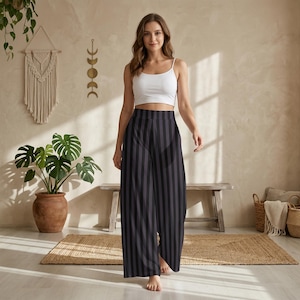May include: A white sleeveless camisole top paired with high-waisted, wide-leg trousers featuring vertical black and dark gray stripes. The trousers have a relaxed fit and a clean, straight-cut silhouette that extends to the floor.
