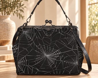 May include: A black handbag featuring a white spiderweb pattern across the front. The bag has a dark metal frame, a kiss-lock closure with two spheres, a top handle, and a detachable shoulder strap with metal hardware attachments on the sides.