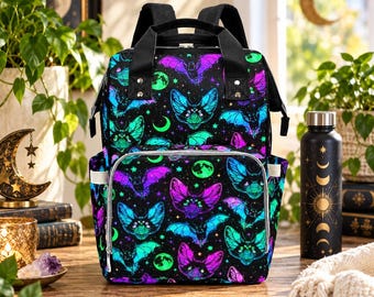 May include: A black backpack featuring a vibrant neon pattern of bats, crescent moons, and stars in shades of purple, blue, and green. The bag includes a top handle, adjustable shoulder straps, a front zippered pocket, and side pockets.