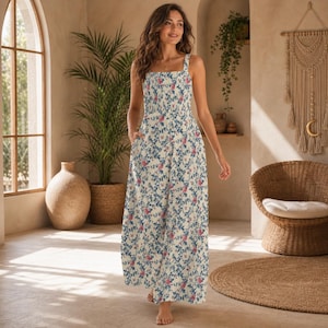 Könnte beinhalten: Ein ärmelloses, bodenlanges Kleid mit quadratischem Ausschnitt und einem Blumenmuster aus blauen und rosa Blüten auf cremefarbenem Hintergrund. Das Kleid hat Taschen und eine lockere Passform.