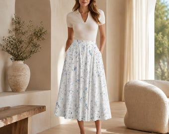 Puede incluir: Una camisa de manga corta color crema con cuello en V combinada con una falda midi blanca con un delicado estampado floral azul. La falda tiene un corte de cintura alta y una silueta acampanada que cae por debajo de las rodillas.