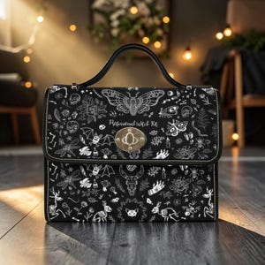A structured black handbag with a top handle and a gold twist-lock closure, featuring a white moth pattern.