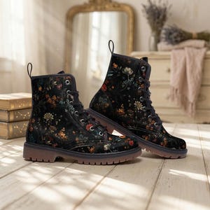 Może przedstawiać: Para czarnych butów bojowych z kwiatowym wzorem w odcieniach czerwieni, pomarańczy, żółci i bieli. Buty mają czarne sznurowadła i brązową podeszwę. Buty mają około 15 cm wysokości.