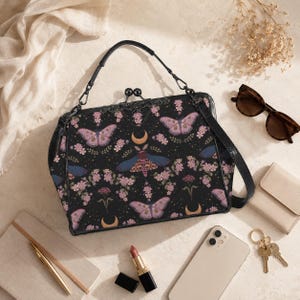 Puede incluir: Bolso de mano negro con un estampado floral y de mariposas. El bolso tiene un asa superior y una correa para el hombro. Otros artículos incluyen gafas de sol, una cartera, un teléfono, llaves y pintalabios.