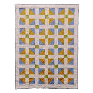 May include: A handmade quilt with a repeating pattern of yellow and blue triangles set against a white background. The quilt is bordered with a light blue fabric and features green square accents. The overall design is geometric and symmetrical.