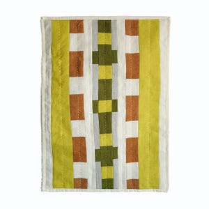 May include: A rectangular quilted textile wall hanging featuring vertical stripes in shades of lime green, burnt orange, off-white, and olive green. The central column displays a repeating block pattern of olive green and light gray squares.
