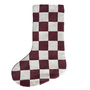 May include: A Christmas stocking featuring a repeating chequered pattern in deep burgundy and off-white. The fabric has a visible woven texture, and the stocking is shaped with a traditional heel and toe, presented against a plain white background.
