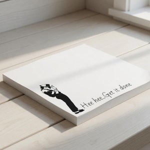 May include: A white square notepad with a black and white cartoon illustration of a person bending over. The text "Hee hee...Get it done" is printed in black on the notepad.