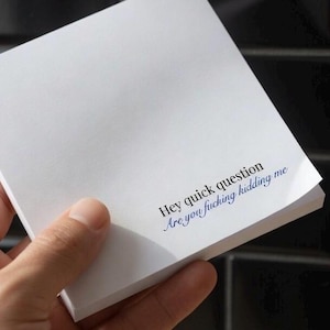 May include: A stack of white notepaper with the text "Hey quick question Are you fucking kidding me" printed in blue. The notepaper is held by a hand.
