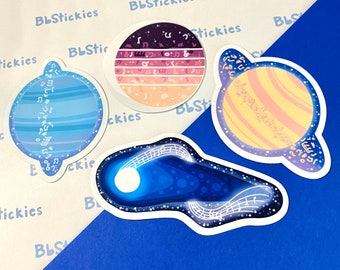 May include: Four stickers with musical designs. One is a blue planet with musical notes, another a comet with a musical staff, and two are planets with musical notes and a sunset colour scheme. The text "BbStickies" is repeated.