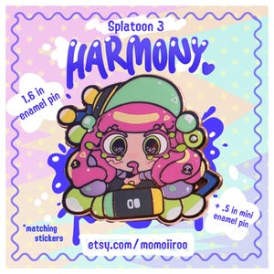 May include: Enamel pin featuring a cartoon character from Splatoon 3, with pink hair and a green hat. The pin is 1.6 inches in size and includes the word "HARMONY". The design is set against a pastel background with the text "etsy.com/momoiiroo".