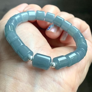 May include: A light blue bracelet with rectangular beads and silver accents. The bracelet is made of polished, translucent stones. The beads are strung together with a flexible cord. The bracelet is a piece of jewelry.