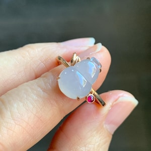 May include: A ring featuring two white jade gourds with a small red gemstone accent. The ring is made of gold and has a delicate design.