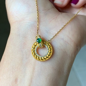 May include: A gold chain necklace with a circular pendant featuring a green gemstone and small clear stones around the edge.