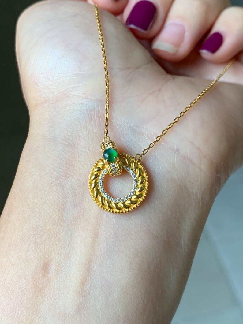 May include: A gold chain necklace with a circular pendant featuring a green gemstone and small clear stones around the edge.