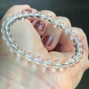 May include: A clear quartz crystal beaded bracelet. The bracelet is made of round, smooth beads that are strung together on a clear elastic cord.
