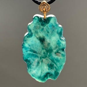 May include: A teal blue resin pendant with a gold-tone bail. The pendant is shaped like a flower with a textured surface.