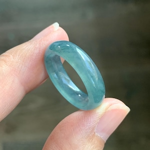 May include: A smooth, polished ring crafted from translucent jadeite stone, featuring a rounded band profile. The material displays a vibrant, semi-transparent teal and blue-green coloration with natural internal cloud-like inclusions throughout.