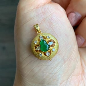 May include: A gold pendant with a green jade stone and clear rhinestones. The pendant is in the shape of a flower.