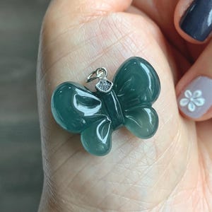 May include: A teal-colored butterfly pendant with a silver bail. The pendant is carved from a translucent material, showcasing the intricate details of the butterfly's wings. The butterfly pendant is a jewelry item.