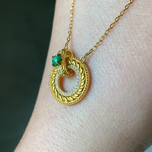 May include: A gold chain necklace with a circular pendant featuring a green gemstone and a detailed design of small white stones.