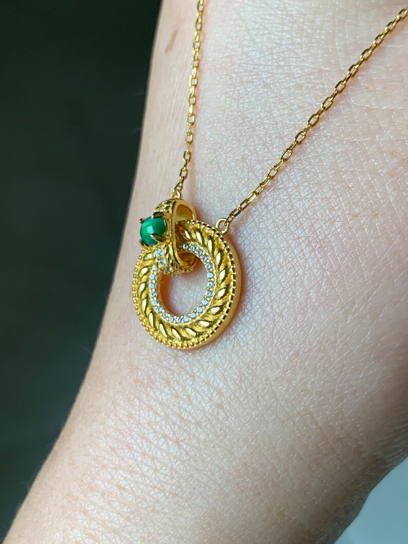May include: A gold chain necklace with a circular pendant featuring a green gemstone and a detailed design of small white stones.