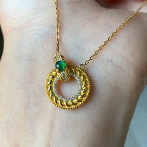 May include: A gold necklace with a circular pendant featuring a green gemstone and small clear stones around the edge.